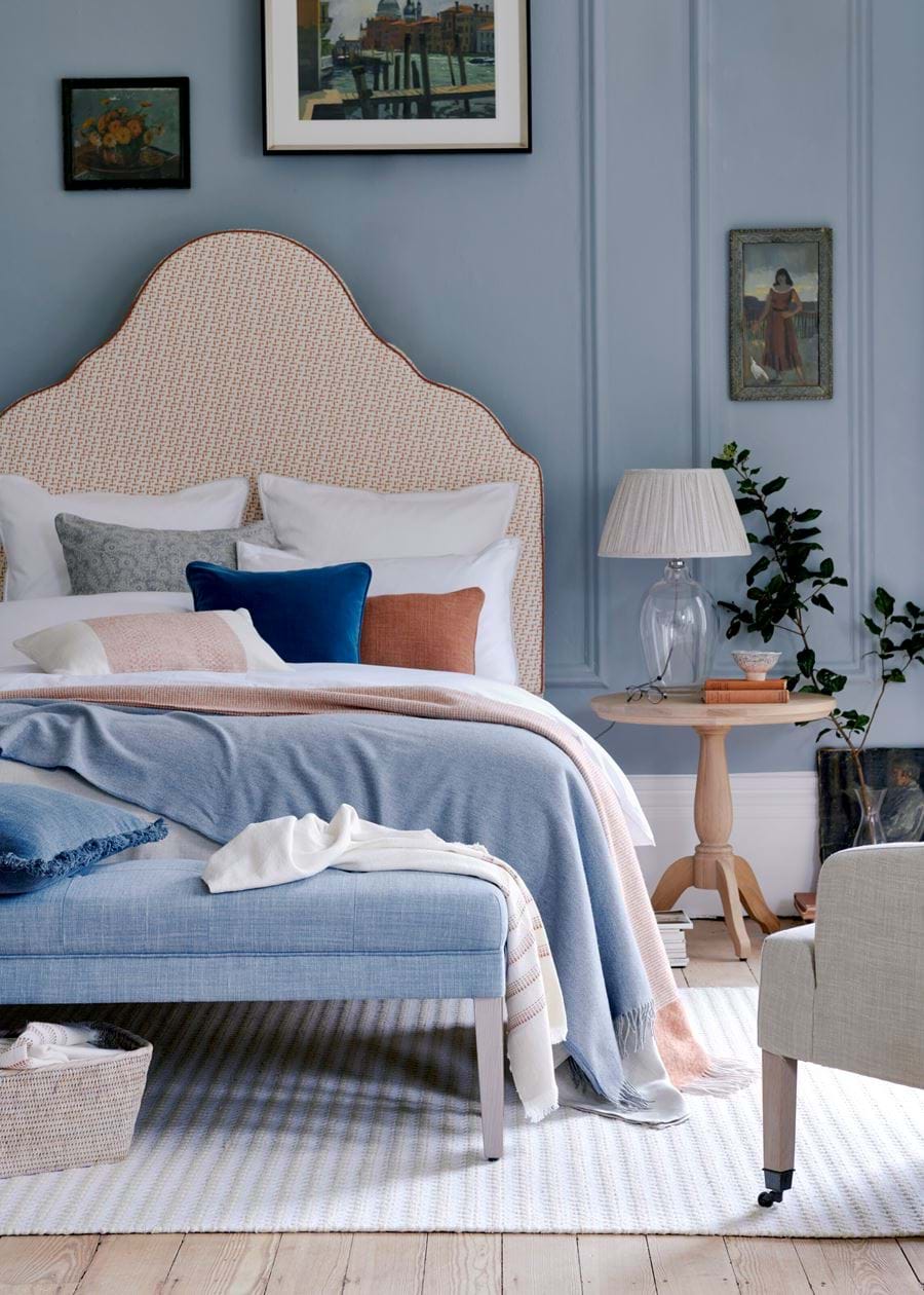 Oversized statement headboard upholstered in pale coral patterned linen.Relaxed linen bedding and Soft Blue walls.